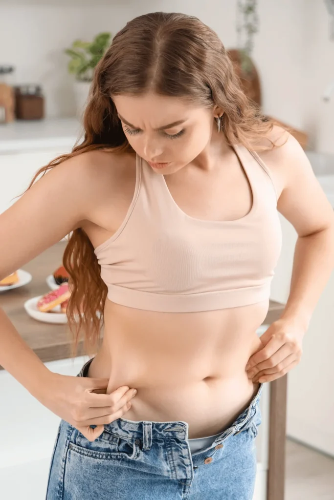 woman looking at her belly while putting on pants